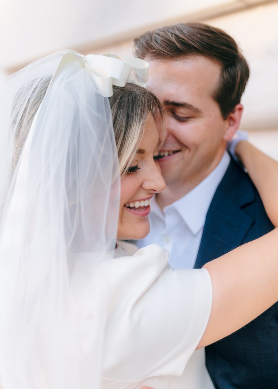 Kristi, in a veil with a satin bow, laughing in the arms of her fiancé
